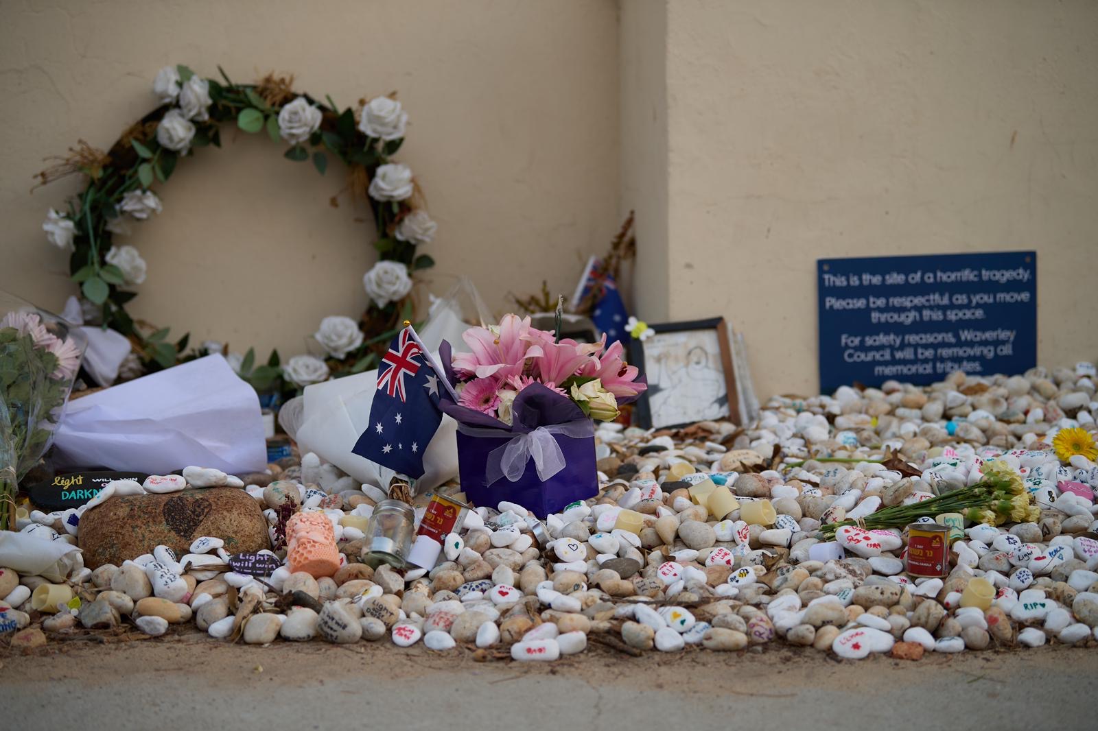 Memorial with flowers, Australian flag, and stones in front of a wall