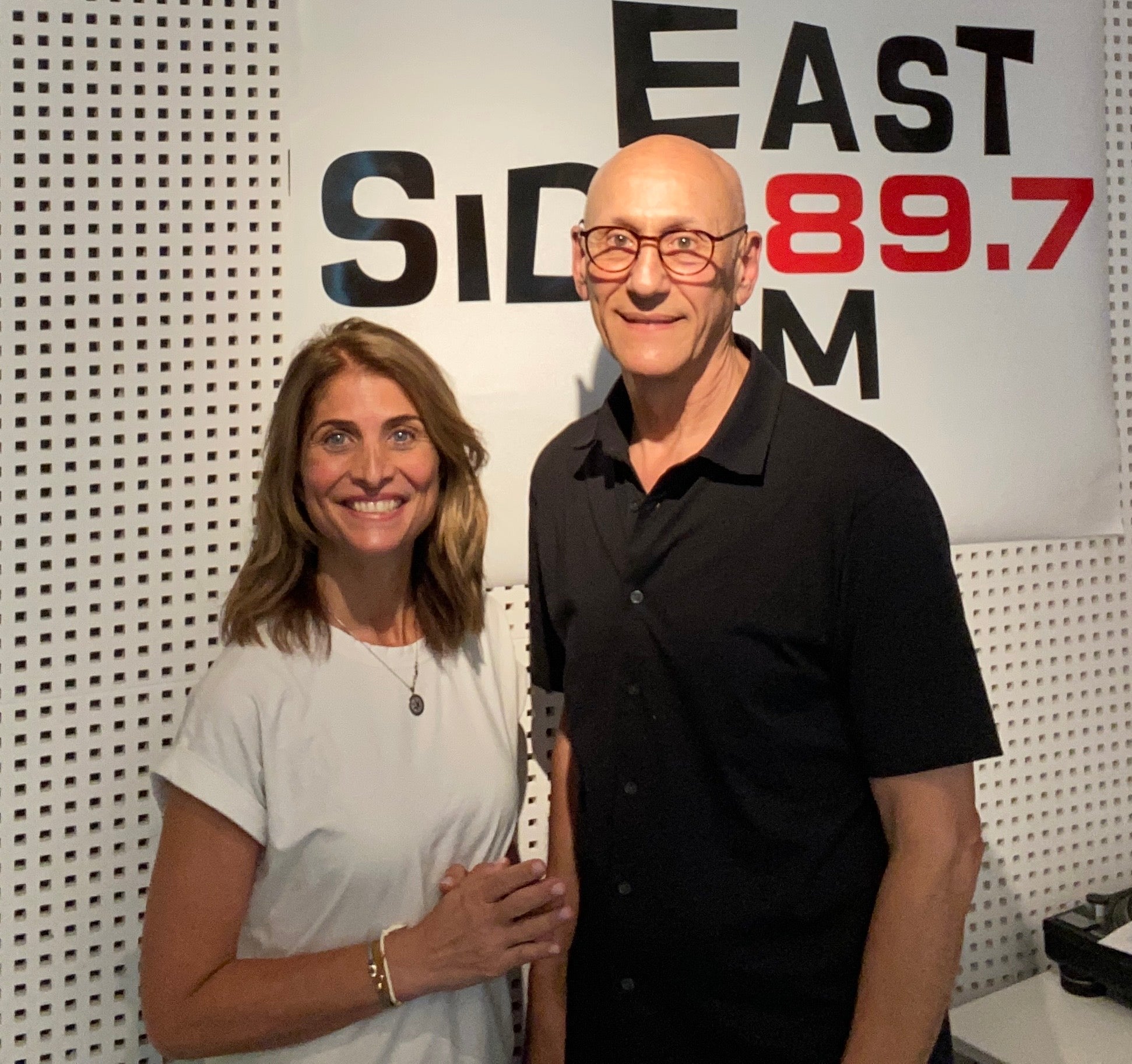 Two people standing in front of an 'East Side 89.7' sign.