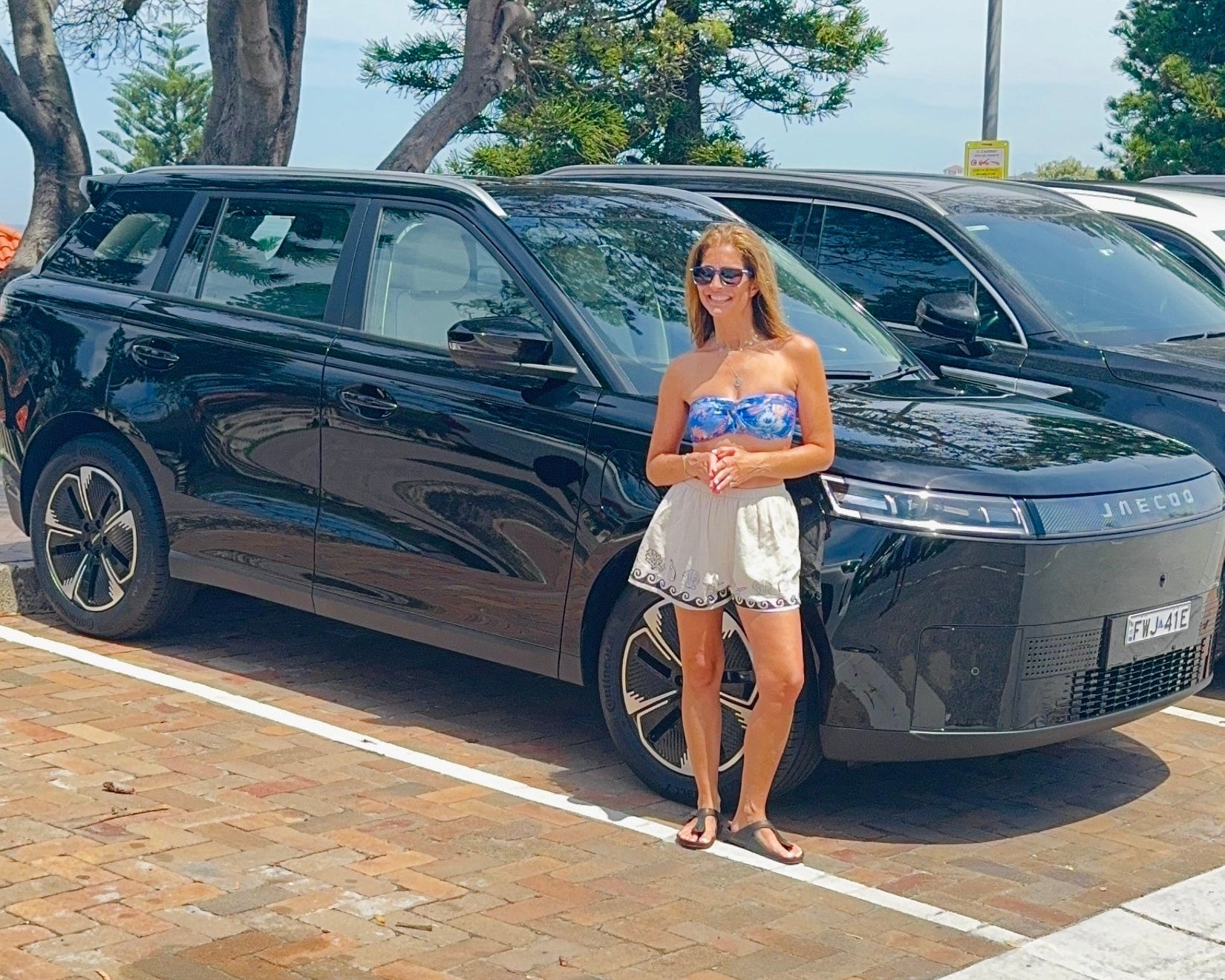 Woman standing next to a black electric car on a sunny day.